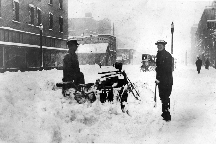 Motorcycle stuck in snow on 9th Street near Idaho Street in 1919. Man on the right is Roy Thompson. McCarty Building on the left. Photo courtesy ISHS 73-205-5