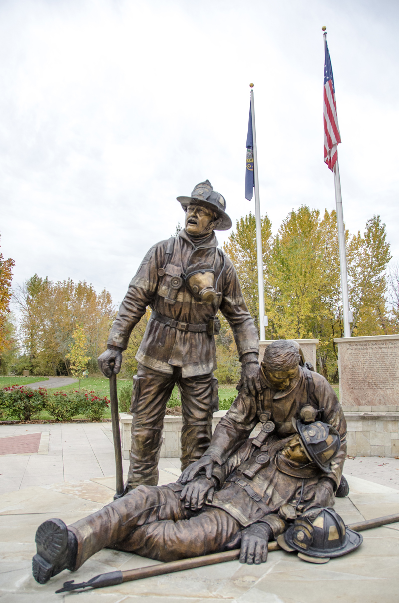 A life-sized bronze sculpture of three firefighters. One lies lifeless in the arms of another. The third stands beside them. 