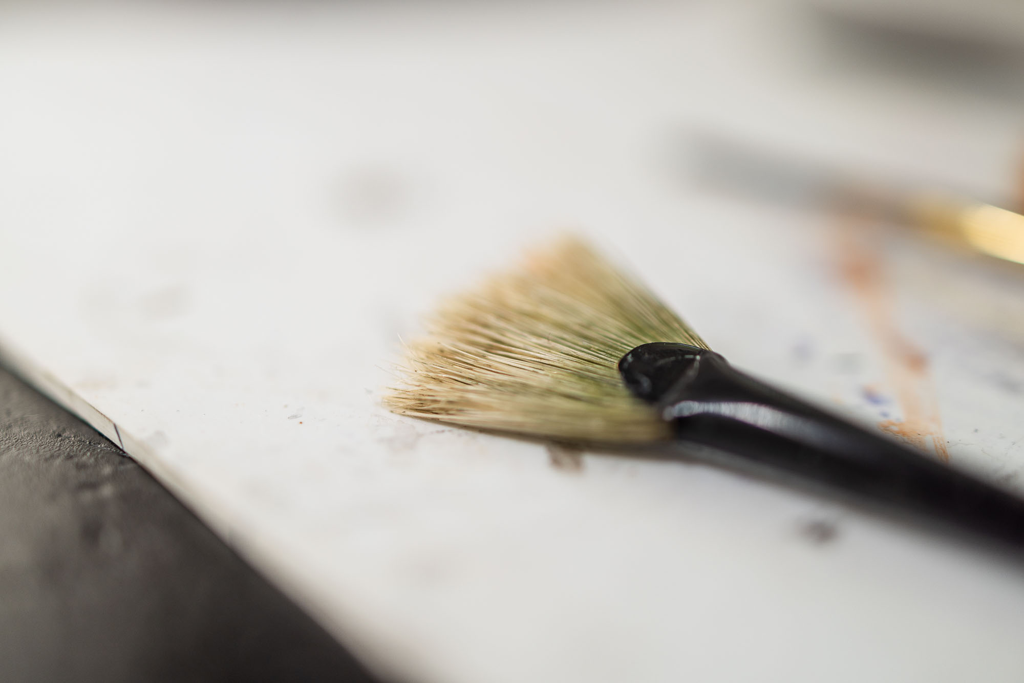 Blurred view of paintbrush laying on white surface.
