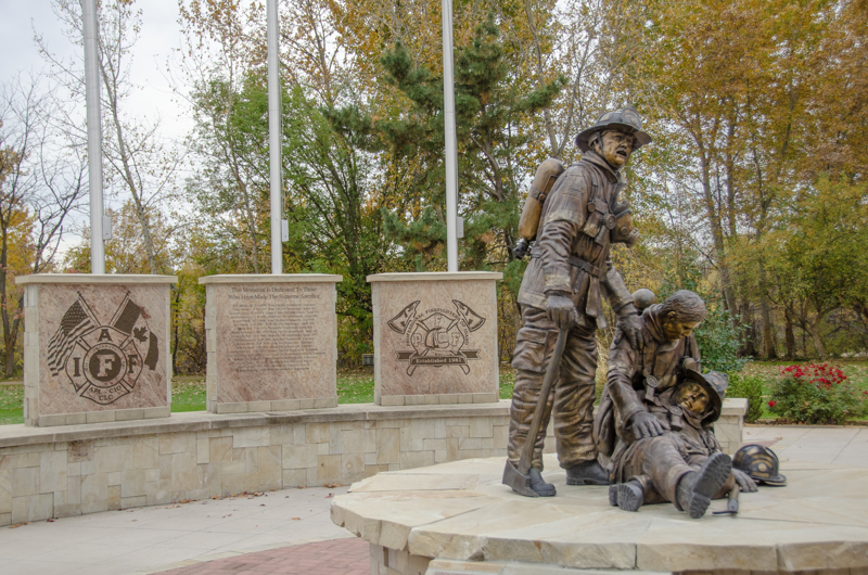 A life-sized bronze sculpture of three firefighters. One lies lifeless in the arms of another. The third stands beside them. 