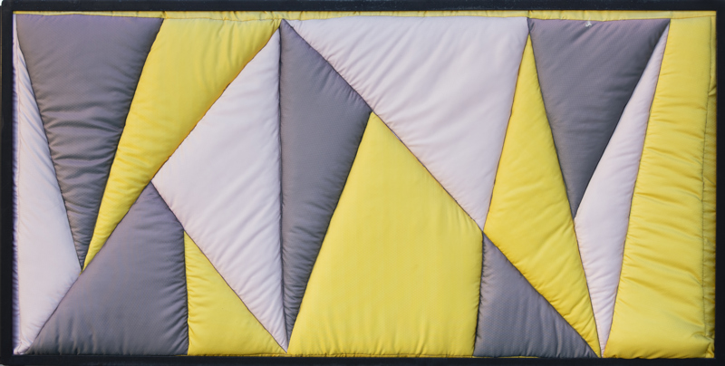 A quilted geometric abstract pieces made up of yellow, grey, and white textile.