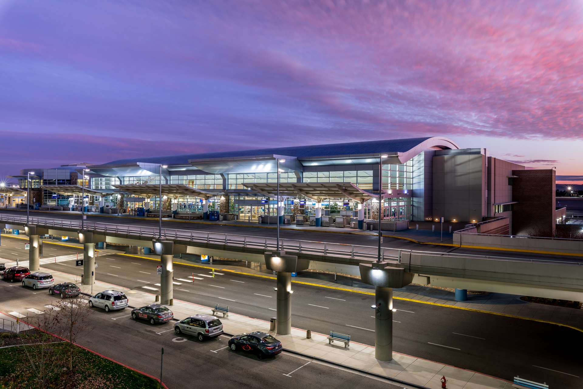 The landside entrance to Boise Airport's curved architecture shines purple and blue at sunset.