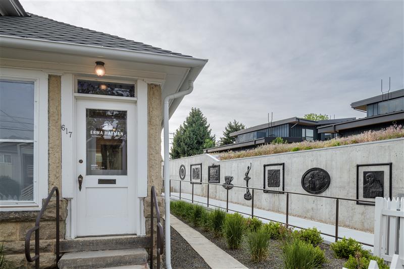 Front door of Erma Hayman House with with art along cement fencing in the background. 