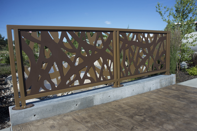 A safety railing made of two layers of brown-painted steel panels cut to resemble the tangled materials used in a beaver dam. 