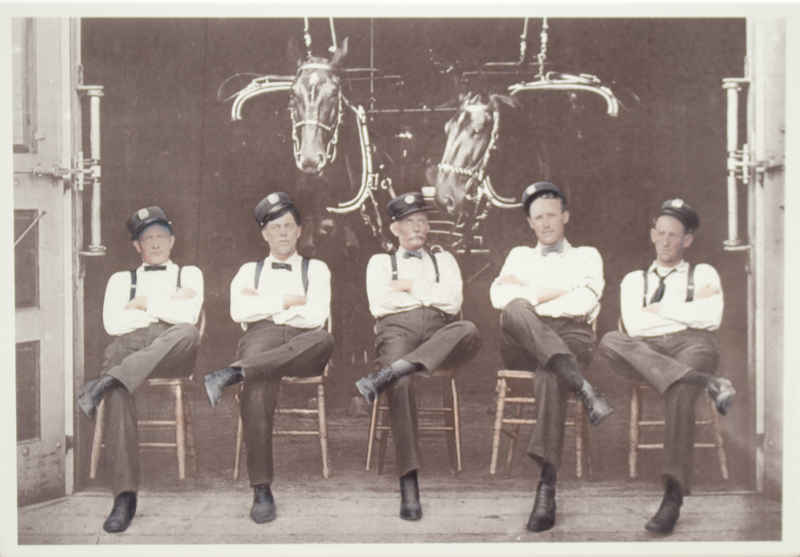 An image of 5 firefighters sitting in chairs in front of 2 horses.