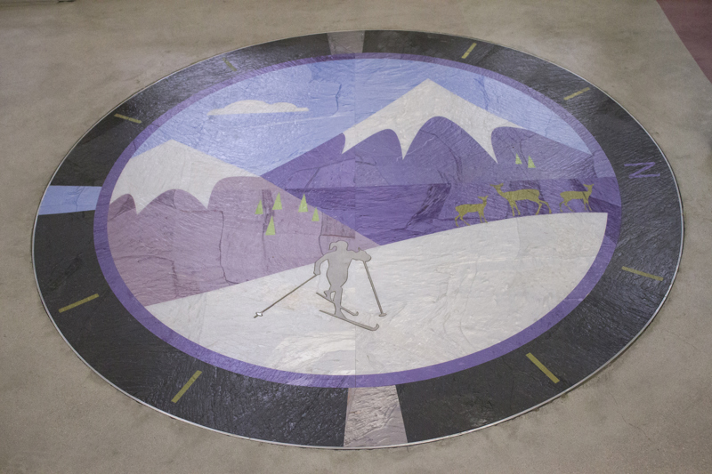 A floor inlay medallion depicting a skier in the Boise Mountains. Around the outside of the medallion are the cardinal directions with the letter N indicating north. 