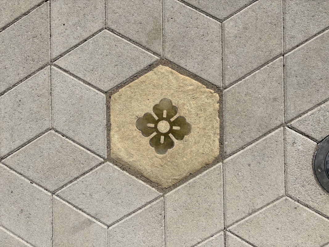 An image of a hexagonal sidewalk paver with a brass inlay of a Japanese symbol.