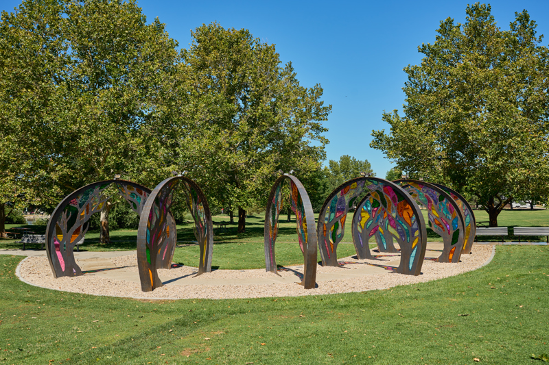 Series of six steel archways with cut tree patterns and colorful acrylic panels covering the voids.