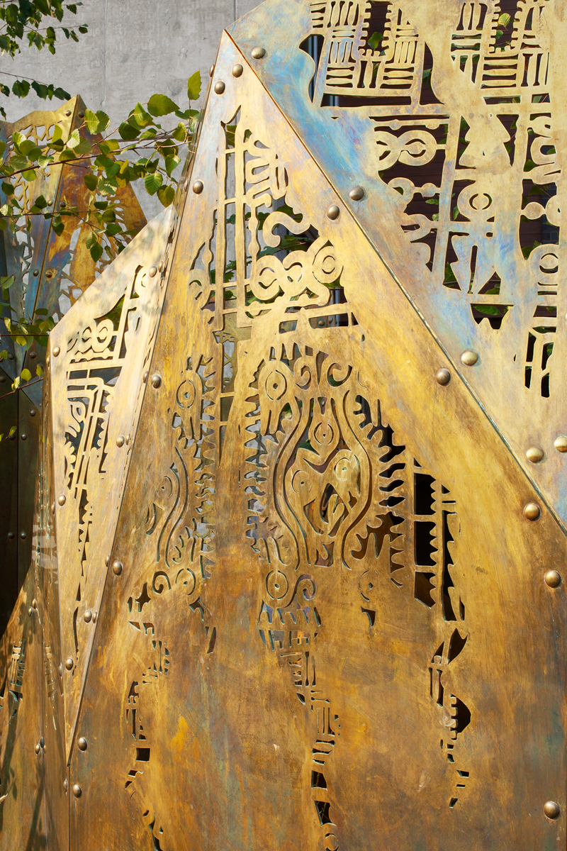A geometric brass sculpture of mountain peaks topped with laser cut fabric patterns from various cultures. 