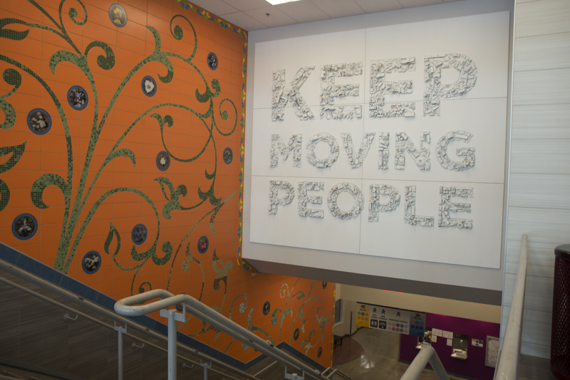A large installation of six panels with the text, "Keep moving people". All text is filled with toys of various vehicles and modes of transportation that have been spray painted white. 
