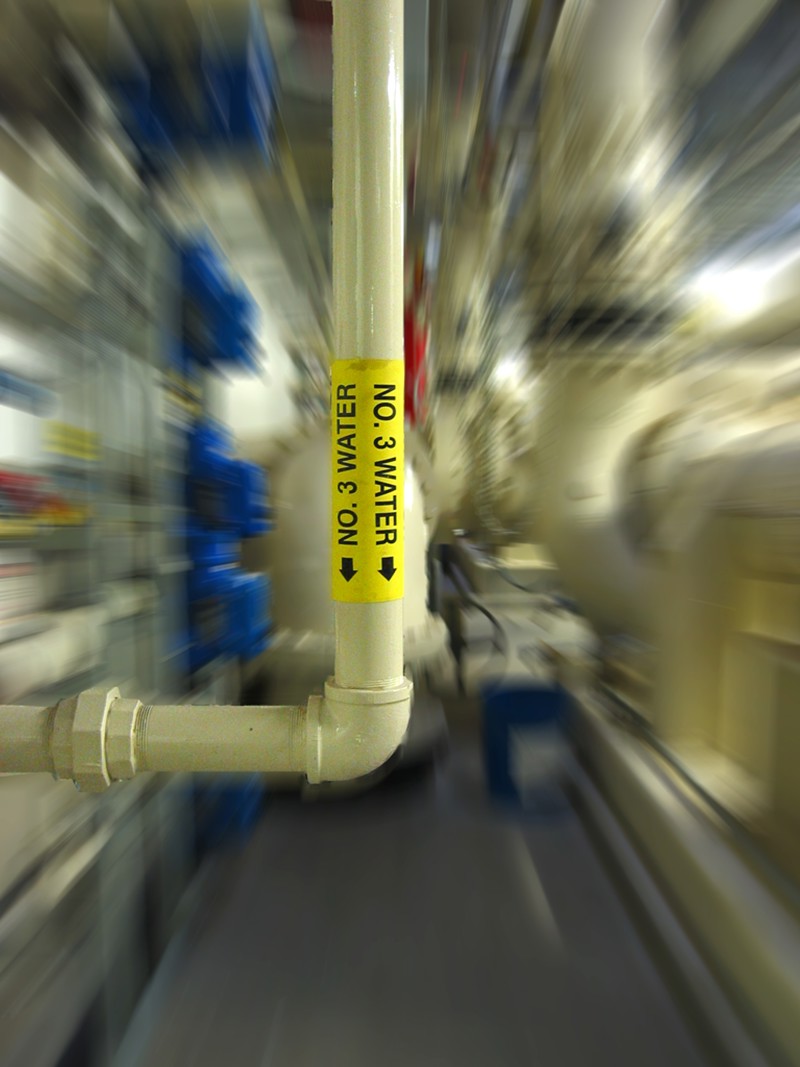 A white bent pipe with a yellow label with the text, "No. 3 Water," with a downward pointing arrow. The image has a zoom effect to look like the view is quickly approaching the pipe.