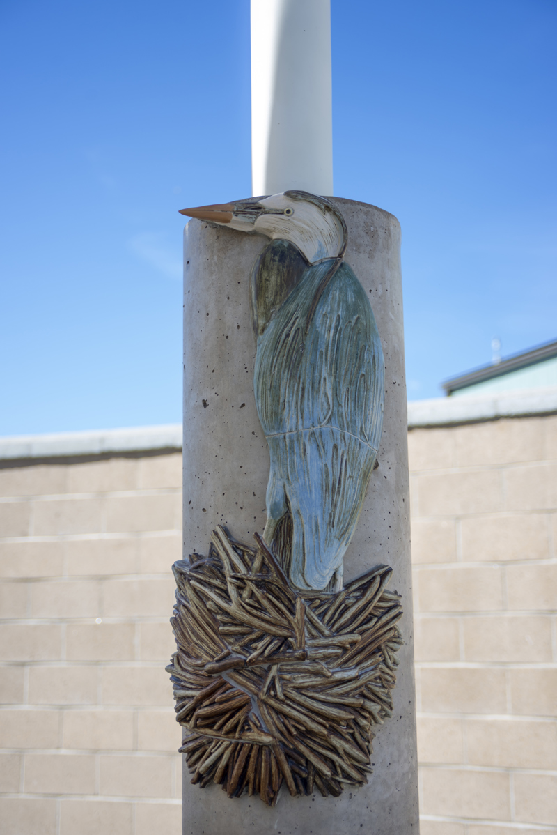 A cement column decorated with a ceramic mosaic relief sculpture of a nesting great blue heron.