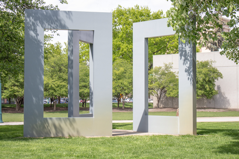 A sculpture of 3 large grey rectangles with open centers, standing like monoliths angled in towards each other.