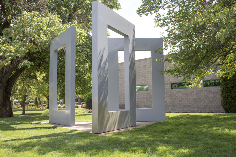 A sculpture of 3 large grey rectangles with open centers, standing like monoliths angled in towards each other.