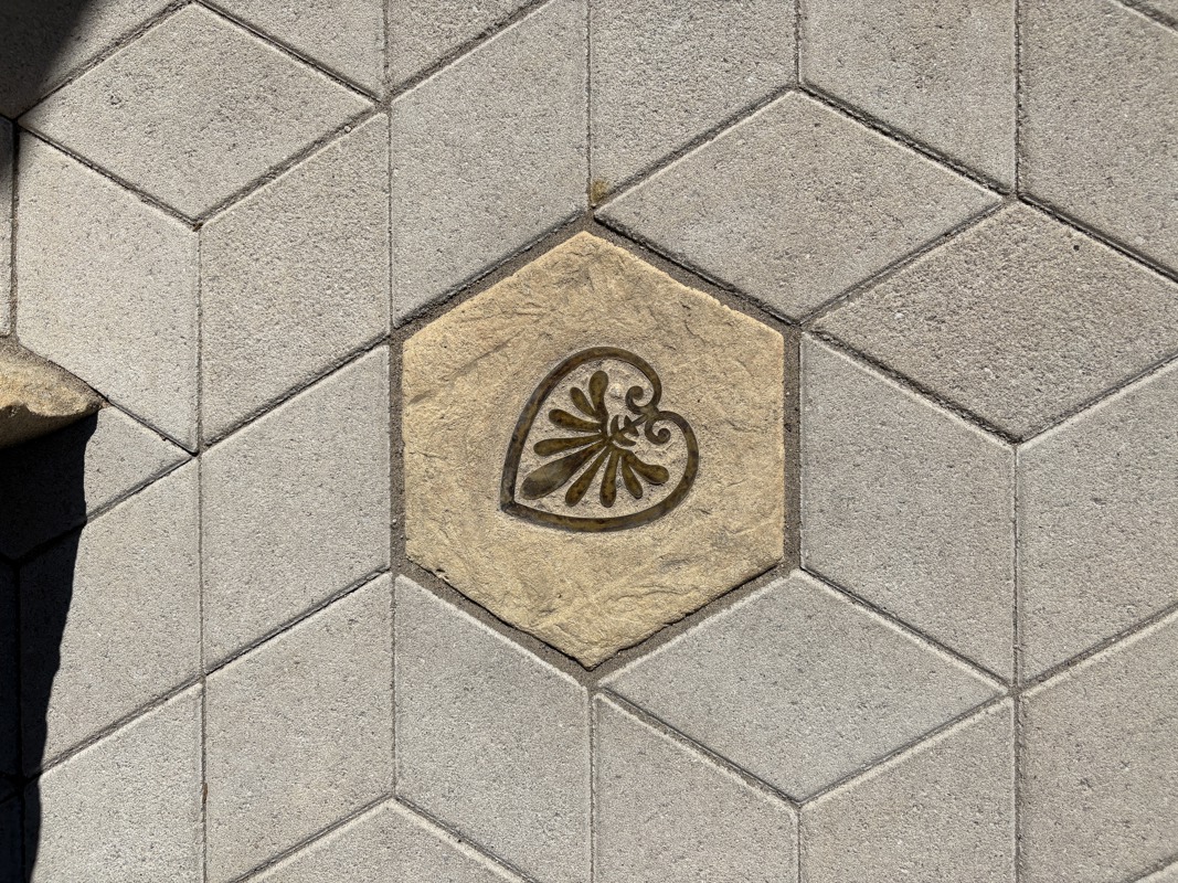 An image of a hexagonal sidewalk paver with a brass inlay of a Greek symbol.