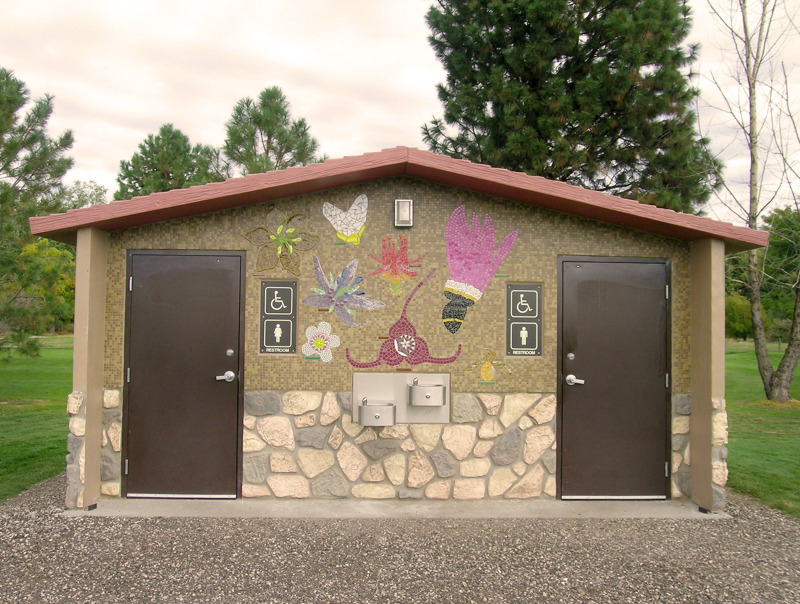 A small park bathroom building with sides covered in tile mosaics depicting flowers found in the state of Idaho. 