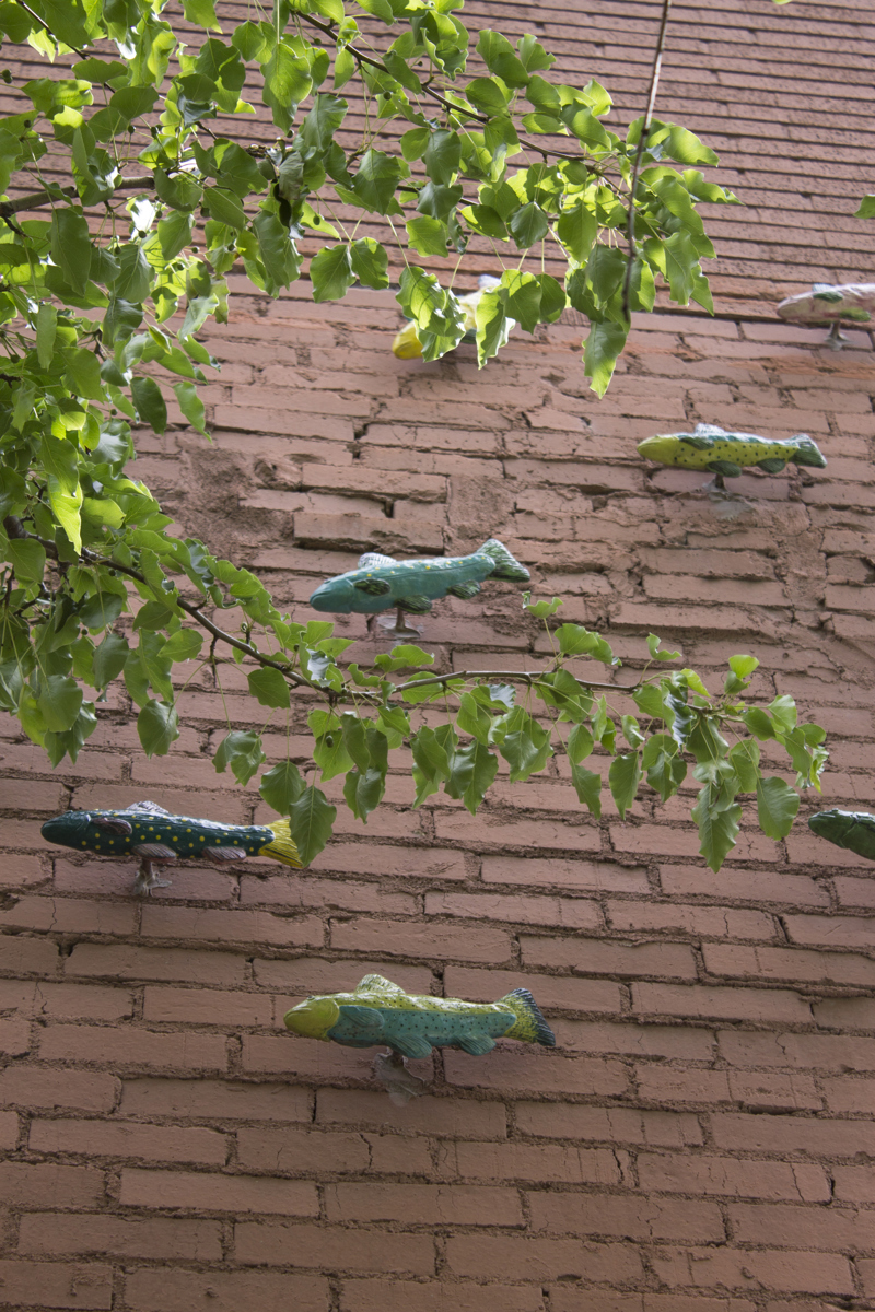 A closeup image of painted ceramic fish sculptures mounted onto a red brick wall, facing right to left.