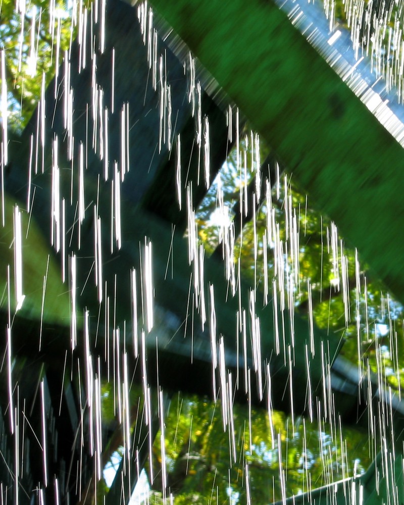 A closeup of water dripping down the green spokes of a waterwheel.