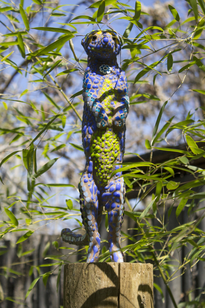 A glass mosaic sculpture of a meerkat standing on a wooden post.