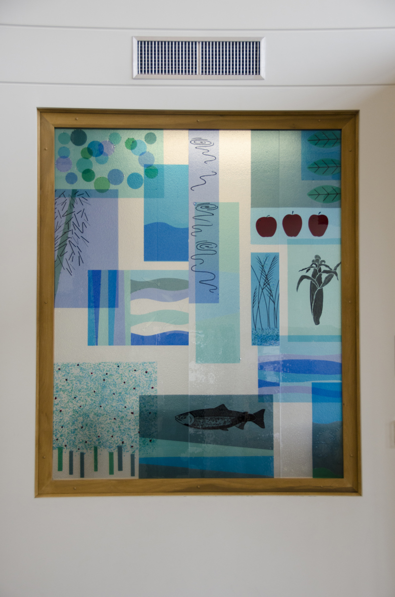 An installation of colorful fired glass pieces in an interior window. On the glass are images of plants and animals that reference the area's agricultural history.