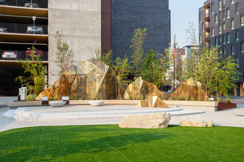 A geometric brass sculpture of mountain peaks topped with laser cut fabric patterns from various cultures. 
