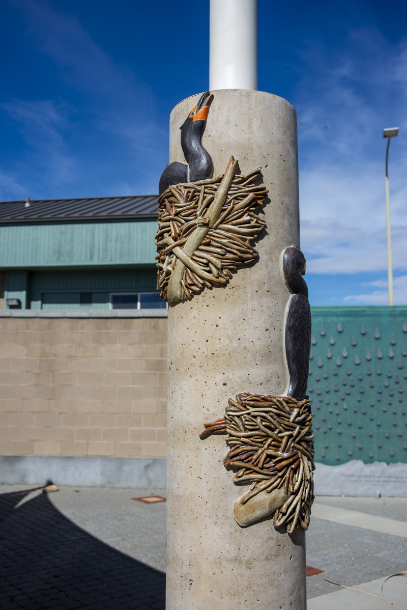 A cement column decorated with two ceramic mosaic relief sculptures of nesting double-crested cormorants.
