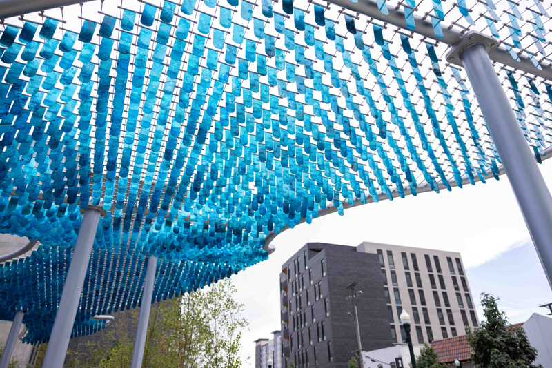 A shade canopy structure consisting of blue, alcohol painted flappers suspended in spanners set between stretched steel cables.
