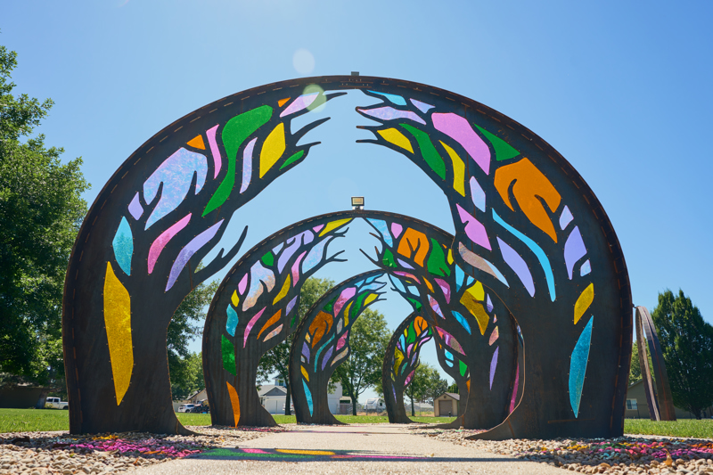 Series of six steel archways with cut tree patterns and colorful acrylic panels covering the voids.