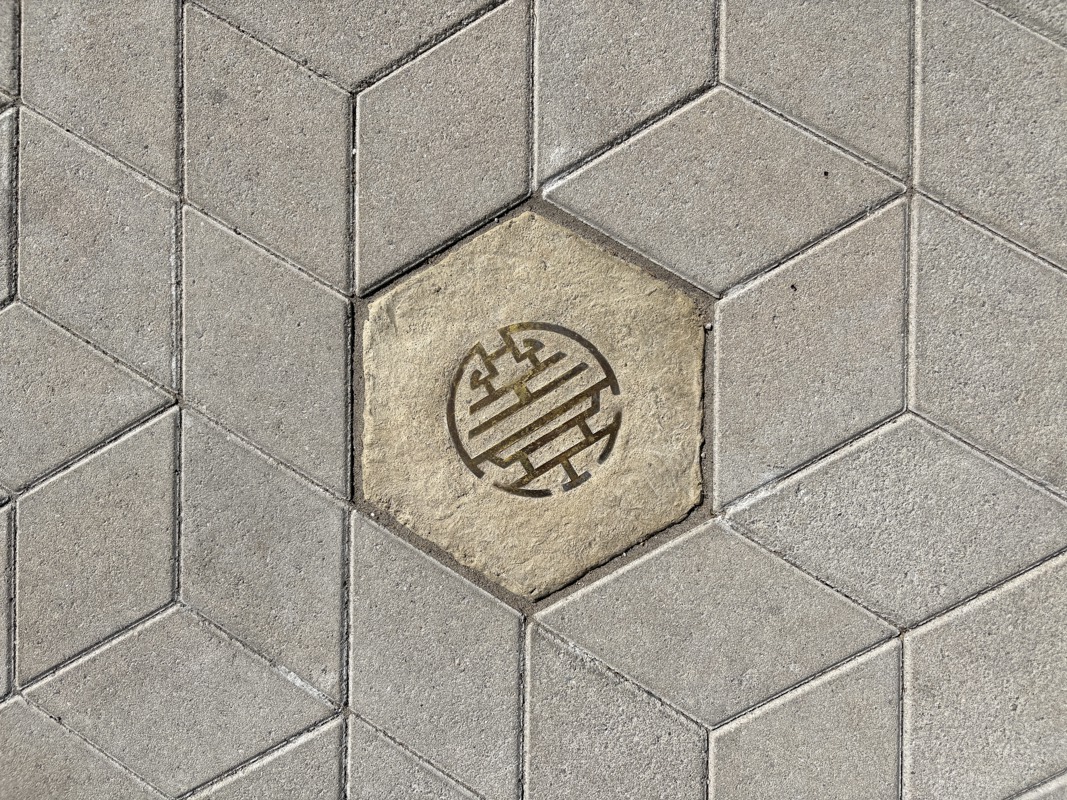 An image of a hexagonal sidewalk paver with a brass inlay of a Chinese symbol.