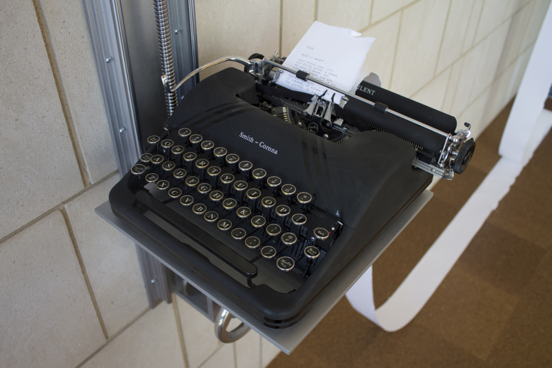An antique typewriter set atop of a shelf that can be raised or lowered along a crankshaft attached to a sandstone wall. The typewriter is fed from a large roll of paper also attached to the wall. The surface of the paper roll features a low-bas relief carving of poplar trees.