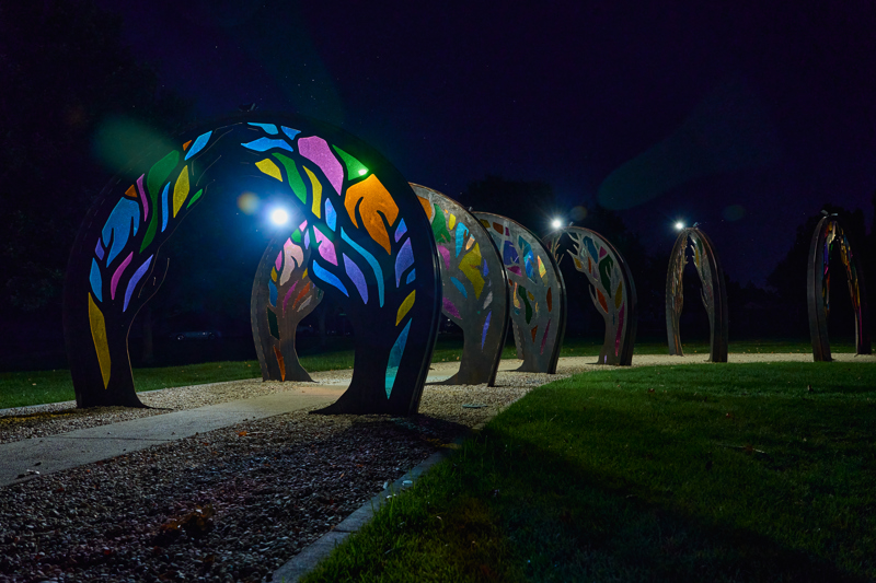 A series of six steel archways with cut tree patterns and colorful acrylic panels covering the voids. Lights mounted to the tops of the arches illuminate the clear acrylic panels.