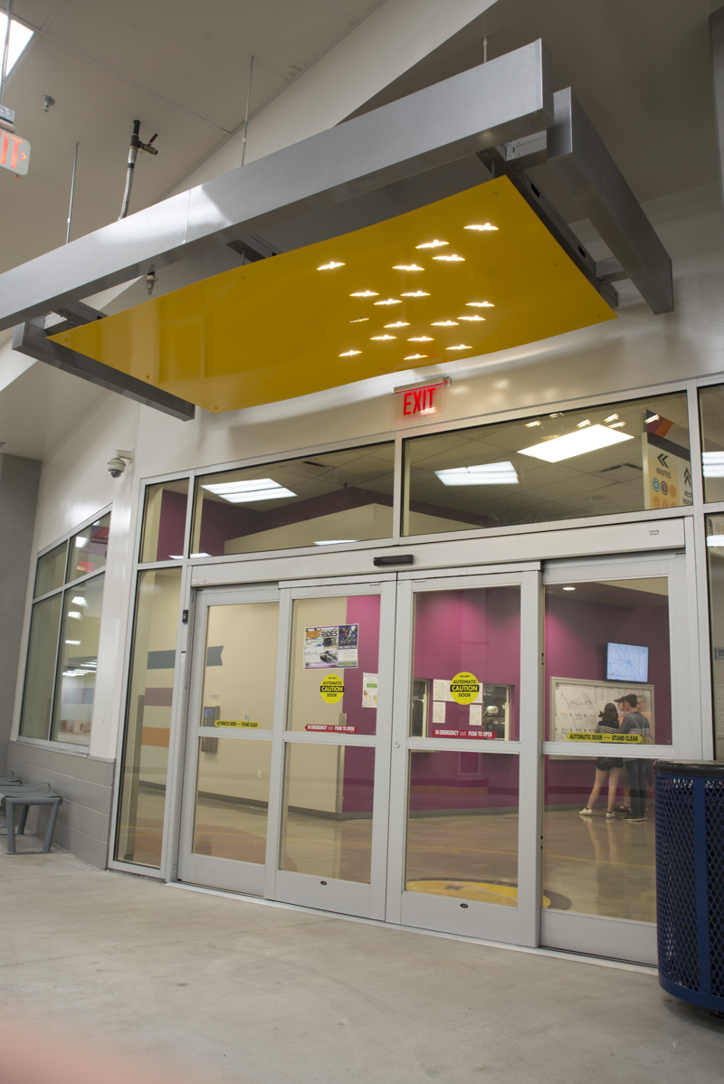 A doorway awning made of painted cut metal. In the awning, lit with backlighting, are holes in the shape of birds.