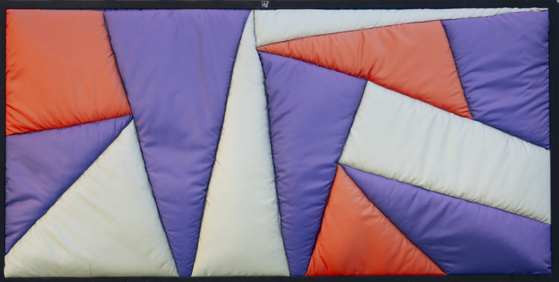 A quilted geometric abstract pieces made up of blue, green, and red textile.