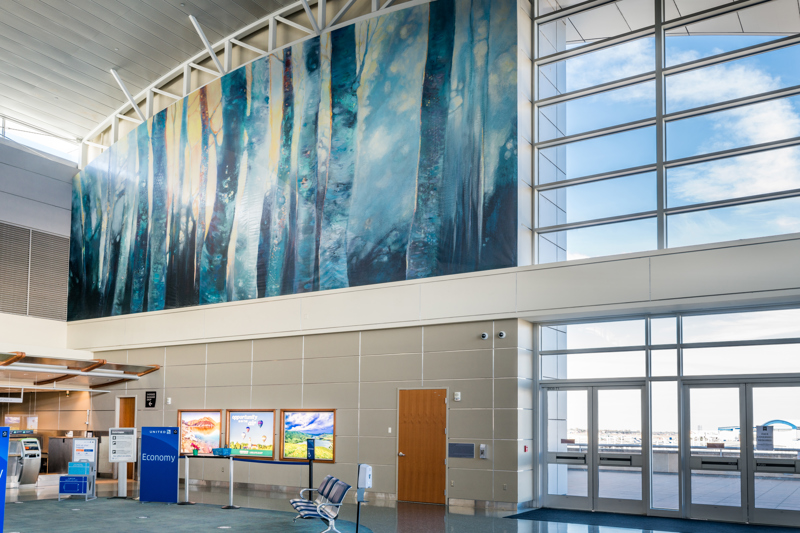 A large vinyl print mural of a series of tree trunks in shades of blue. Behind them is a soft yellow light.