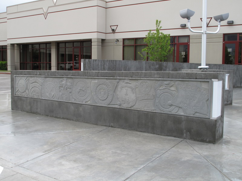 A concrete wall with a low-bas relief sculpture of various badges from Boise's police and fire stations.