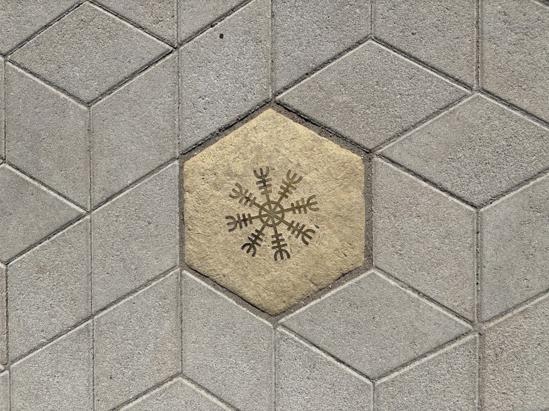 An image of a hexagonal sidewalk paver with a brass inlay of a Scandinavian symbol.