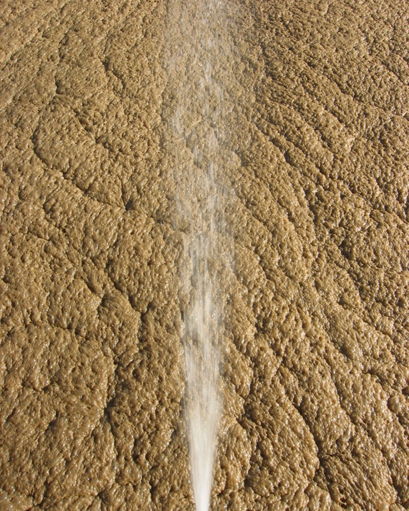 A spray stream of water over a thick layer of brown foamy bubbles.