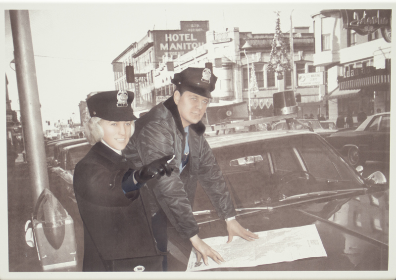An image of a police officer and a meter maid standing next to a parking meter.