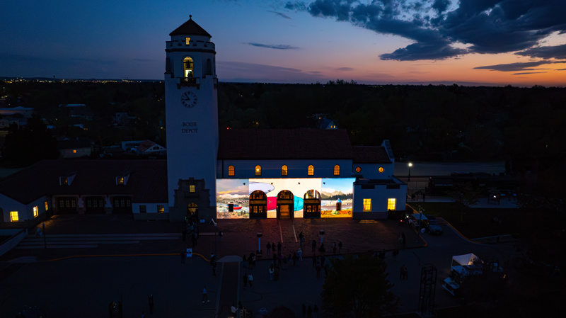 An ariel photograph of the Boise Depot at sunset. On the front of the building is a bright animated projection.