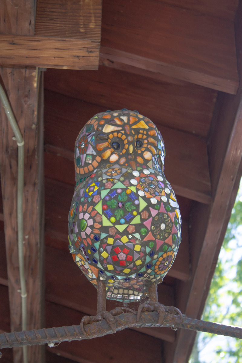 A glass mosaic sculpture of an owl perched on a branch made of metal rebar.