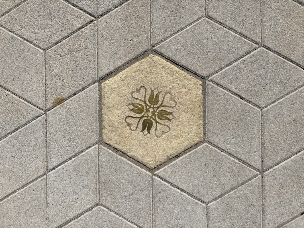 An image of a hexagonal sidewalk paver with a brass inlay of a German symbol.