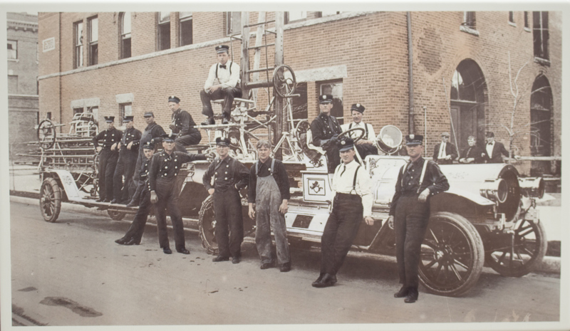 An image of several men standing in front of an engine firetruck from 1912.