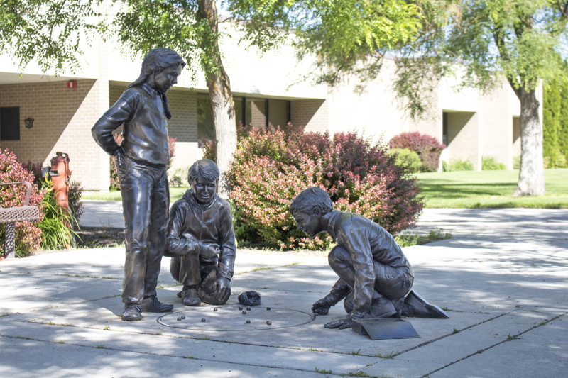 A life-sized bronze sculpture of three young children playing marbles on the sidewalk. 