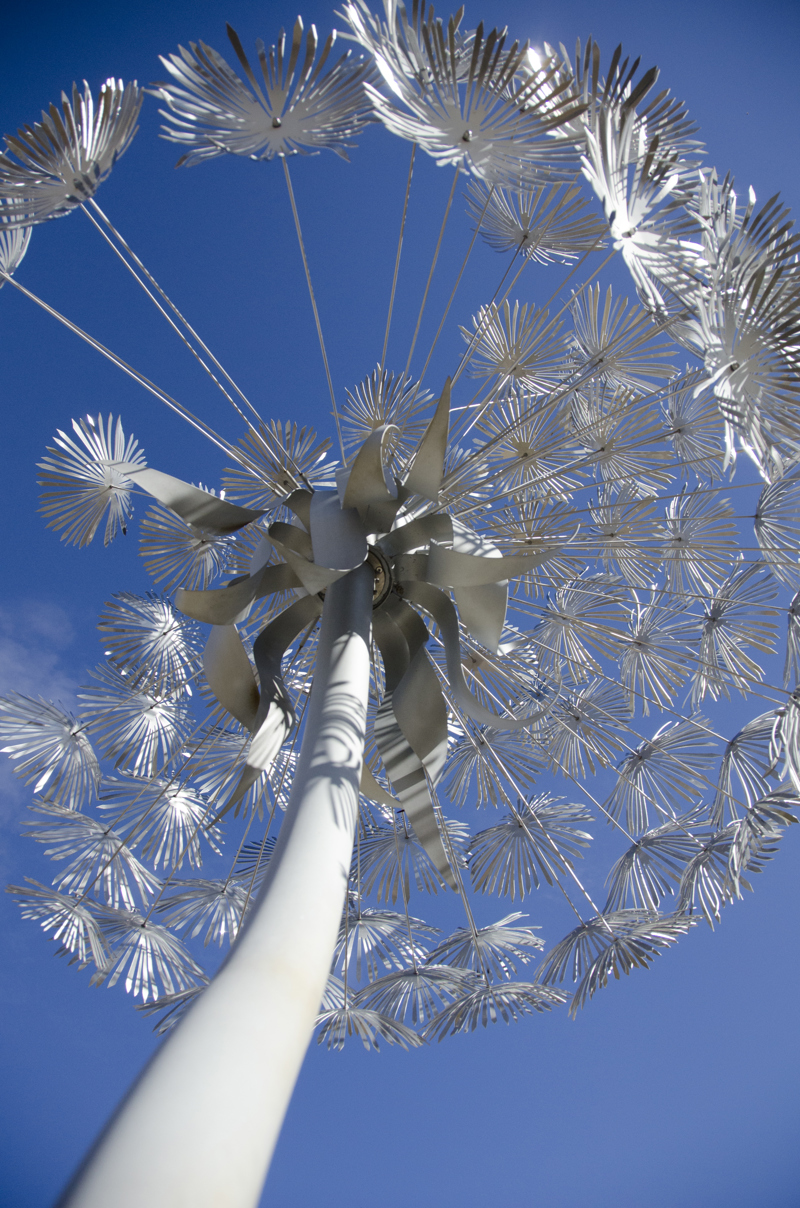 A closeup image of a large stainless steel and aluminum sculpture in the form of a single standing dandelion puff. 